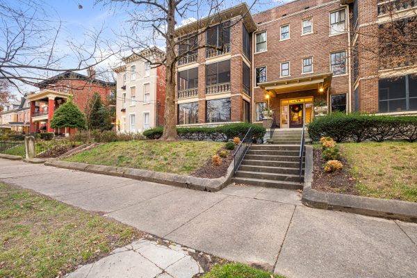 A prime real estate condo in The Highlands of Louisville Kentucky. A large brick home with a lit up front porch and steps leading to the door.