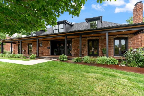 Beautiful, large ranch style home with columns in the front and a spacious green lawn and trees overhanging in the corner